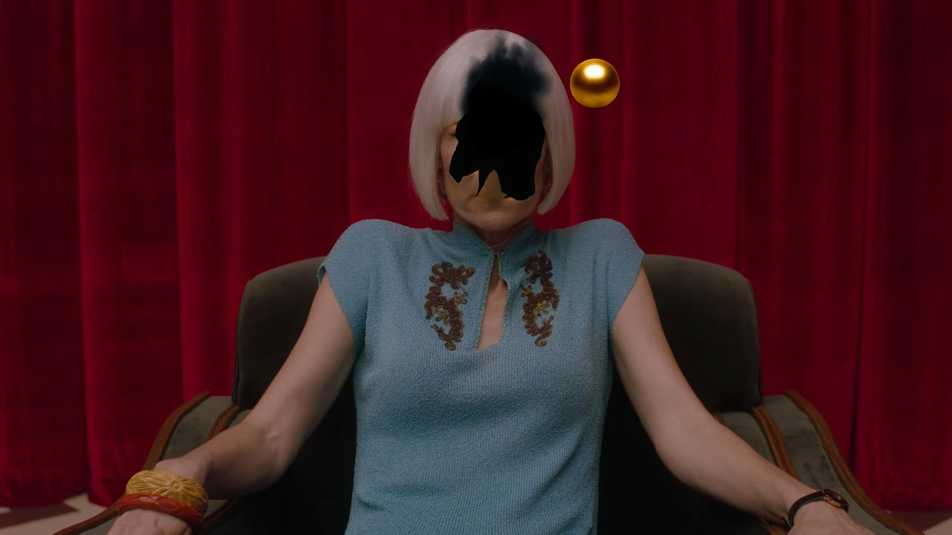 A doubled figure seated before red curtains in Twin Peaks: The Return